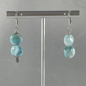May include: A pair of silver dangle earrings with two light blue round gemstone beads on each earring.