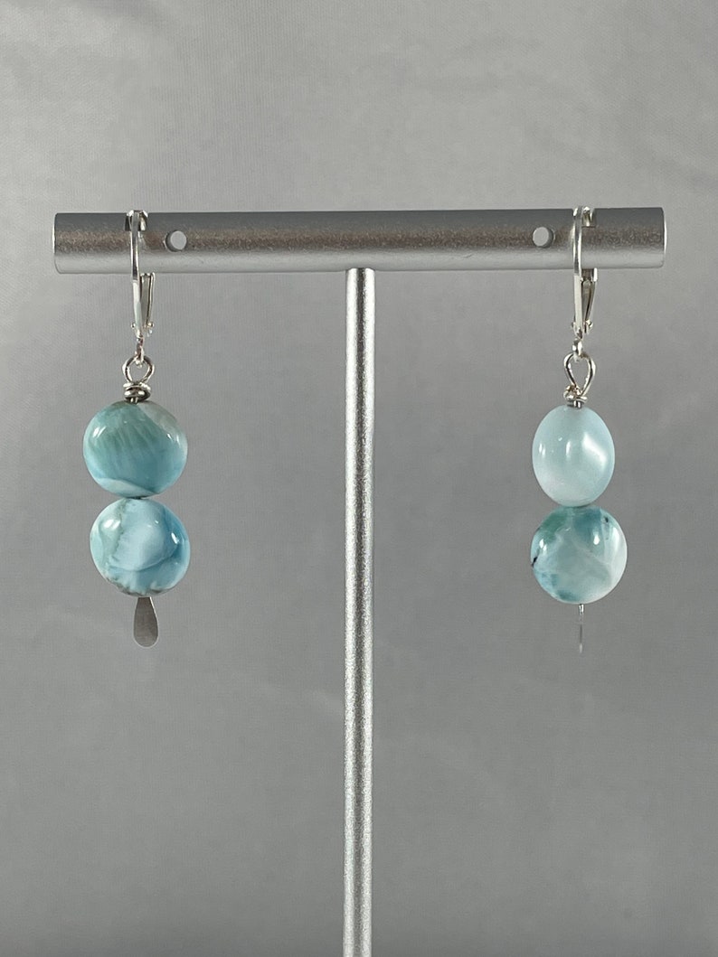 May include: A pair of silver dangle earrings with two light blue round gemstone beads on each earring.