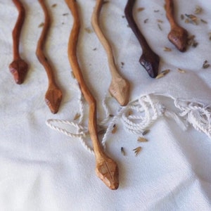 以下が含まれることがあります： 白い布の表面に置かれた、彫刻された頭を持つ木製の蛇の形をした棒が5本。棒は長さも茶色の濃淡も様々です。