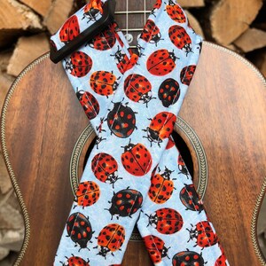 May include: A ukulele strap with a light blue background and a repeating pattern of red and black ladybirds.