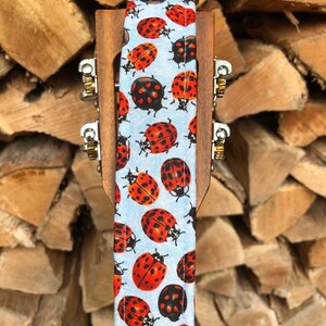May include: A light blue guitar strap with a pattern of red and black ladybirds.