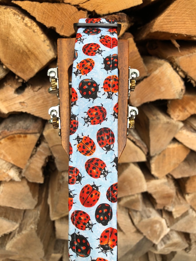 May include: A light blue guitar strap with a pattern of red and black ladybirds.