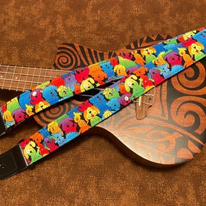 May include: A colorful guitar strap with a pattern of cartoon dogs. The strap is made of fabric and has black leather ends.