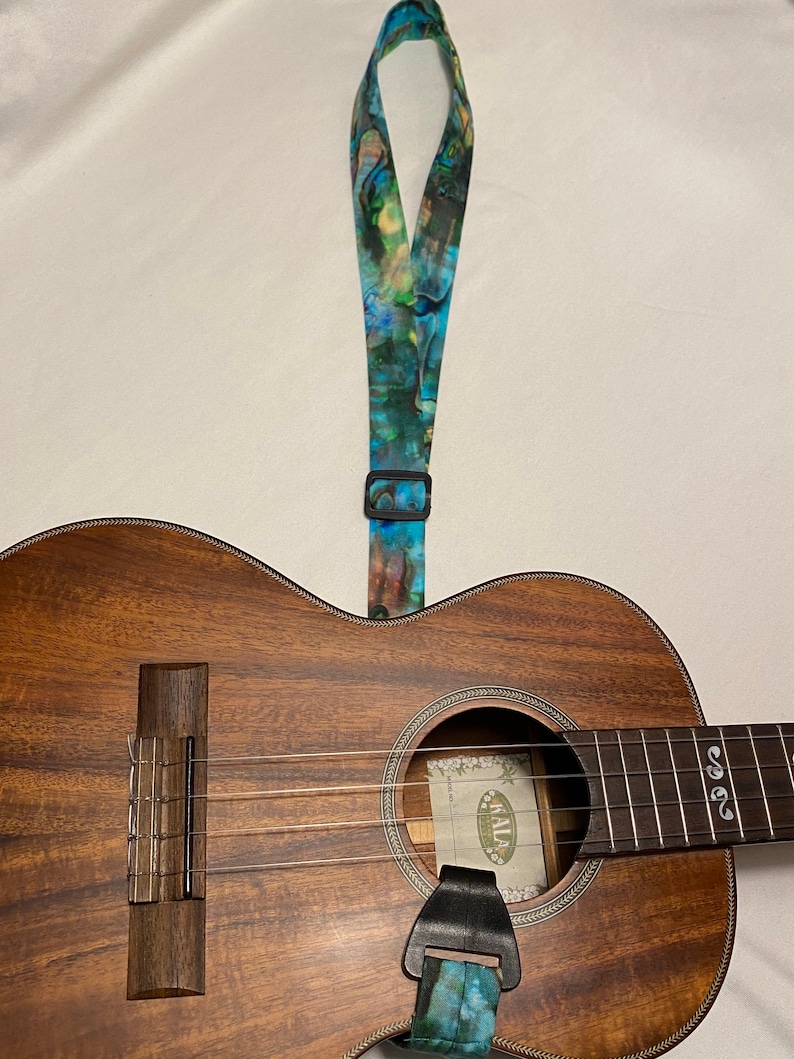 May include: A brown ukulele with a blue and green patterned strap. The ukulele has a sound hole with a label that says "Kala".