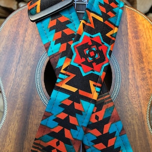 May include: A ukulele with a colorful geometric patterned guitar strap. The strap is black, orange, blue, and white.