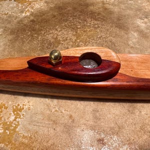 Pode incluir: Um cachimbo de madeira artesanal com acabamento em dois tons. O cachimbo apresenta uma tigela marrom avermelhada escura e uma base de madeira clara e natural. Uma pequena peça de metal dourado é fixada no topo. O cachimbo é projetado para fumar.