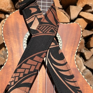 May include: A black ukulele strap with a brown and gold tribal pattern. The strap is wrapped around a ukulele.