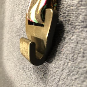 May include: A black plastic hook with a floral patterned strap attached. The hook is designed to be used as a clip or a hanger.