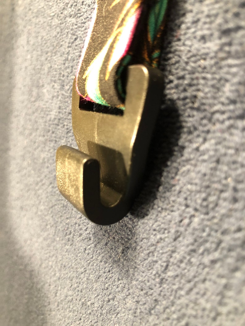 May include: A black plastic hook with a floral patterned strap attached. The hook is designed to be used as a clip or a hanger.