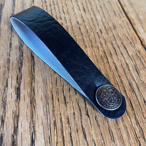 May include: A black leather strap with a silver metal button. The button has a decorative design.