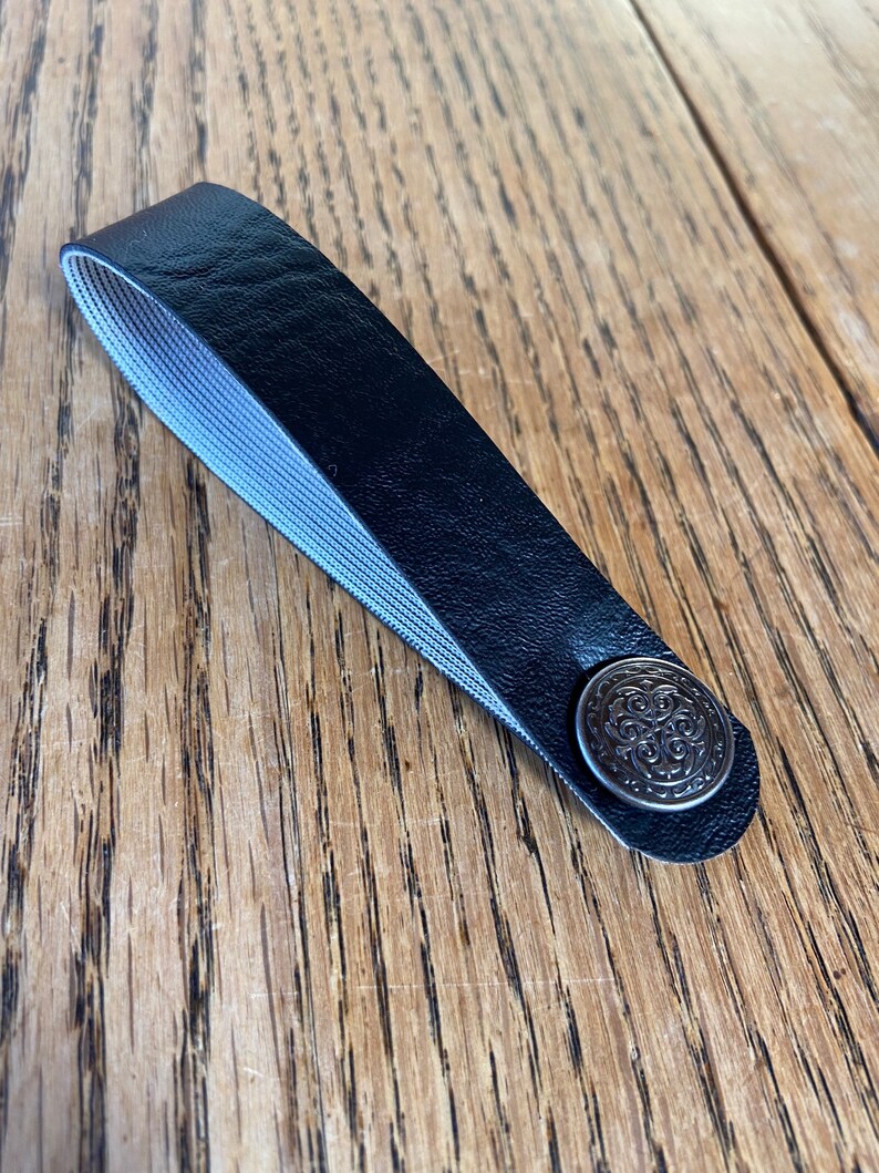 May include: A black leather strap with a silver metal button. The button has a decorative design.