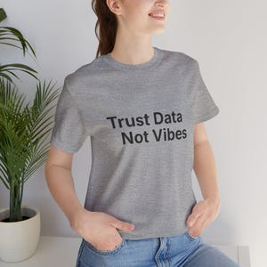 Può includere: T-shirt grigio melange con la scritta nera "Trust Data Not Vibes". La maglietta è a girocollo.