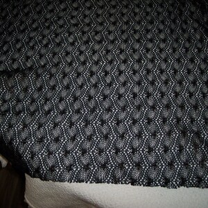 May include: A black fabric textile featuring a repeating openwork crochet pattern. The material displays a consistent geometric mesh design with interconnected circular motifs throughout the entire surface of the dark, lightweight, and semi-sheer fabric.
