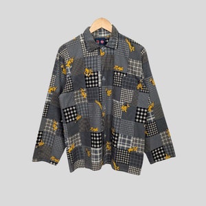 Könnte beinhalten: Ein langärmliges Hemd mit Knöpfen und Patchwork-Muster. Das Hemd ist aus weichem, bequemem Stoff und hat verschiedene Farben und Muster, darunter Schwarz, Weiß und Grau. Das Hemd ist mit einem Cartoon-Hundemuster verziert.