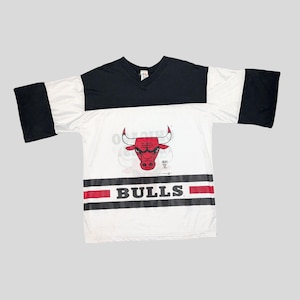 Könnte beinhalten: Weißes und schwarzes T-Shirt mit kurzen Ärmeln mit einem rot-schwarzen Chicago Bulls Logo und dem Wort "BULLS" in schwarzen Buchstaben.