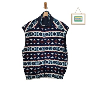 Könnte beinhalten: Eine marineblaue Fleeceweste mit einem geometrischen Muster in Weiß, Rot und Grün. Die Weste hat einen Reißverschluss und einen Stehkragen.