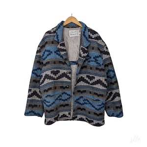 Op de afbeelding: Een blauw en grijs gepatroneerd wollen jack met een knoopsluiting en een Simon's label. Het jack heeft een ontwerp in southwestern stijl.