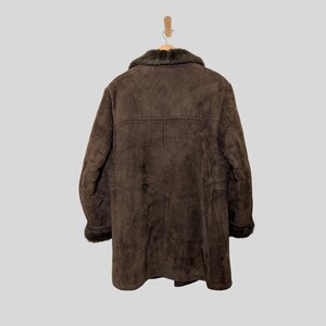 May include: A brown suede coat with a faux fur collar and trim, hanging on a wooden hanger. The coat has a long length and a classic design, suitable for cold weather. The coat is made of a soft, textured material.