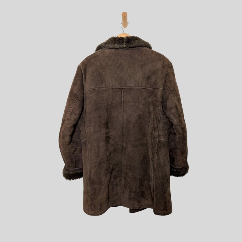 May include: A brown suede coat with a faux fur collar and trim, hanging on a wooden hanger. The coat has a long length and a classic design, suitable for cold weather. The coat is made of a soft, textured material.