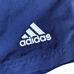 以下が含まれることがあります： 白い刺繍の入ったアディダスロゴが付いたネイビーブルーのショートパンツです。