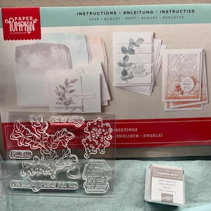 May include: A Paper Pumpkin craft kit box labeled August 2026 with card samples, a clear photopolymer stamp set featuring botanical designs and text, and a small square Gray Granite Stampin' Spot ink pad inside a cardboard shipping container.