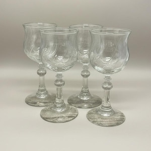 May include: Four clear glass goblets with ornate stems and flared bowls. The bowls feature a swirling design. The goblets are arranged on a light-coloured surface, showcasing their elegant form. Ideal for serving wine or other beverages.