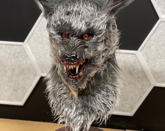 May include: A gray and white werewolf bust with red eyes and a snarling expression. The bust is mounted on a black rotating base with the word "apobob" printed on it.