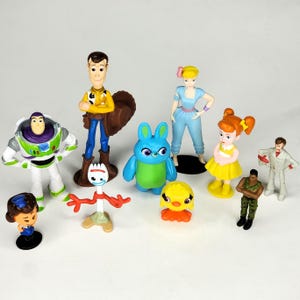 May include: A collection of colorful Toy Story character figurines, including Woody, Buzz Lightyear, Bo Peep, and others. The figures are standing on a white surface. The figurines are made of plastic.