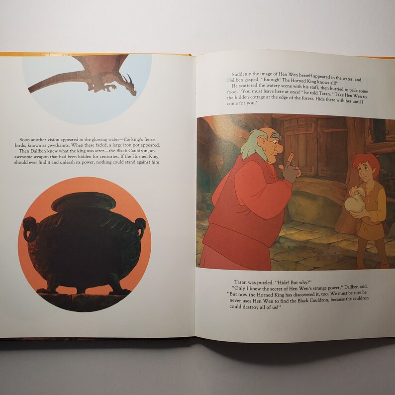 May include: An open book with illustrations from a children's story. One page shows a black cauldron in an orange circle, and a dragon. The other page depicts two characters in a room. Text is visible on both pages.