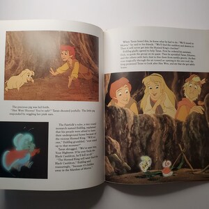 May include: A colorful illustration from a children's book featuring characters in a fantasy setting. The image shows a young man reaching out to a small pig, and a group of people looking out from a cave. Text is included.