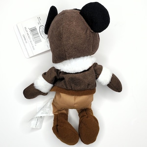 May include: A plush Mickey Mouse Pilot Bean Bag doll, viewed from the back. The doll is dressed in a brown aviator jacket and hat with white trim. The doll has black ears and brown pants. A tag is attached with the text "Pilot Mickey Bean Bag".