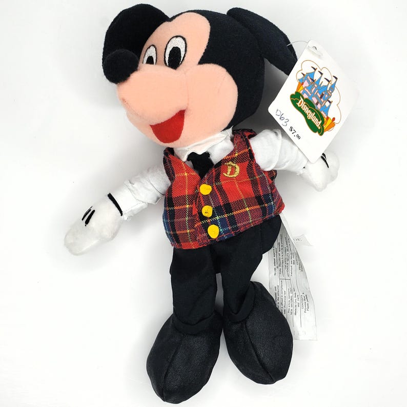May include: A Mickey Mouse soft toy wearing a red plaid waistcoat with yellow buttons, a white shirt, and black trousers. The toy has a pink nose, red mouth, and black ears. A Disneyland tag is attached.