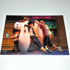 May include: A print featuring characters from the animated film Big Hero 6. The characters are leaning against a large, white, inflatable robot. The background includes a desk, shelves, and other figures.