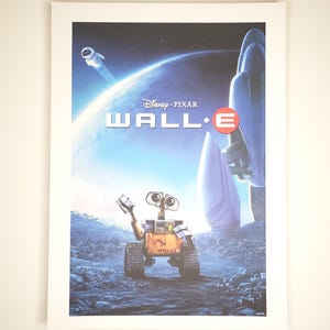 May include: A framed poster for the Disney Pixar film "WALL-E." The poster features the film's title and a depiction of the robot WALL-E on a rocky terrain, with a spaceship and planet in the background. The color palette includes blues, oranges, and whites.