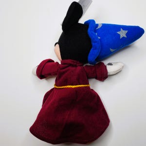 K&ouml;nnte beinhalten: Ein Pl&uuml;schtier einer Figur in einem weinroten Gewand mit einem goldenen Seilg&uuml;rtel und einem blauen Zaubererhut mit silbernen Sternen. Die Figur hat schwarze Ohren, einen schwarzen Kopf und wei&szlig;e Handschuhe.