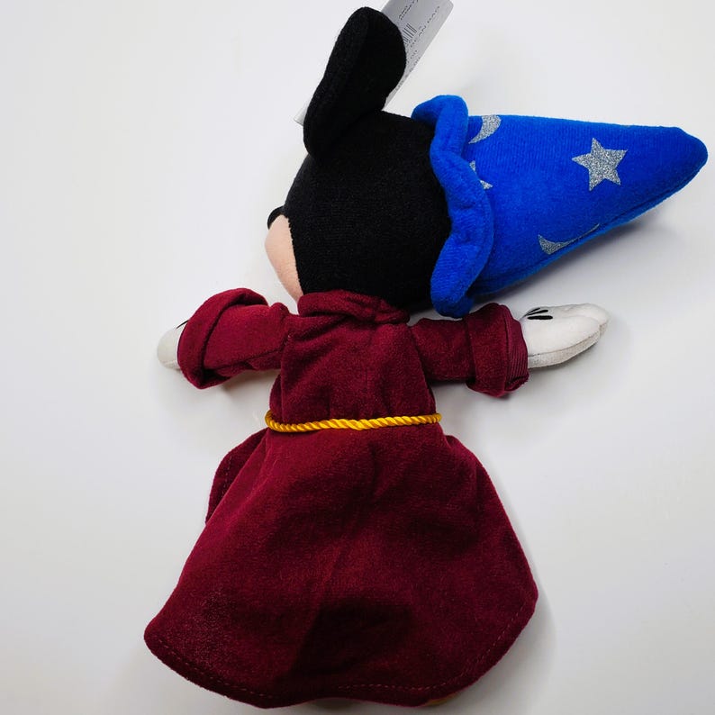 K&ouml;nnte beinhalten: Ein Pl&uuml;schtier einer Figur in einem weinroten Gewand mit einem goldenen Seilg&uuml;rtel und einem blauen Zaubererhut mit silbernen Sternen. Die Figur hat schwarze Ohren, einen schwarzen Kopf und wei&szlig;e Handschuhe.