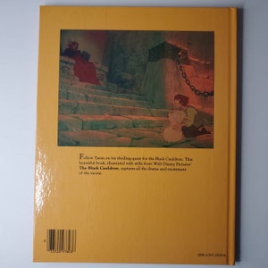 May include: The back cover of a book with a yellow background. The cover features an illustration from Disney's "The Black Cauldron." The image shows a scene with characters and text that reads "Follow Taran on his thrilling quest for the Black Cauldron."