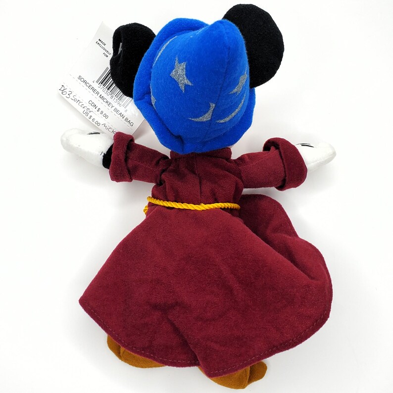 May include: A Sorcerer Mickey Mouse bean bag plush toy. The plush has a blue sorcerer hat with silver stars, a burgundy robe, and yellow rope belt. The toy has black ears, white gloves, and brown shoes. The tag reads "SORCERER MICKEY BEAN BAG".