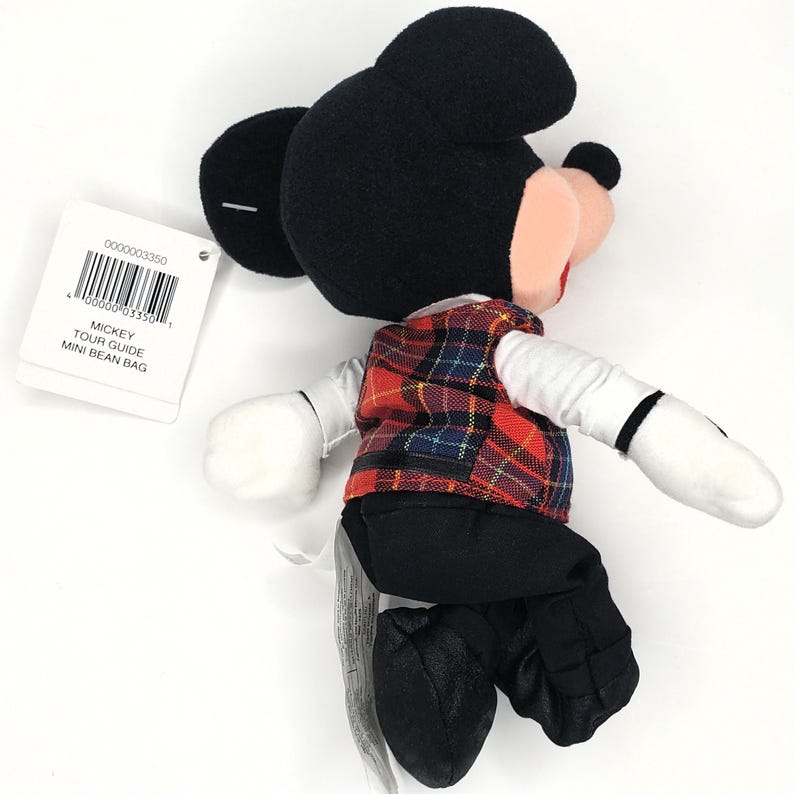 May include: A Mickey Mouse soft toy, dressed in a red, black, and blue tartan waistcoat, black trousers, and black shoes. The toy has black ears, a black head, and white gloves. A tag reads "Mickey Tour Guide Mini Bean Bag."