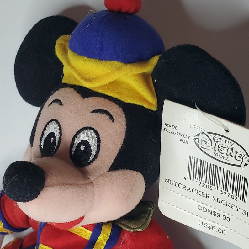 Puede incluir: Un peluche de Mickey Mouse vestido de cascanueces, con una chaqueta roja con ribetes amarillos, un sombrero azul y amarillo con un pomp&oacute;n rojo y una etiqueta blanca que dice MADE EXCLUSIVELY FOR THE DISNEY STORE NUTCRACKER MICKEY BE.
