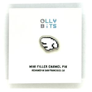 Puede incluir: Una tarjeta blanca con el texto "OLLY BITS" en gris y azul. Un pin plateado con forma de mano pixelada est&aacute; centrado en la tarjeta. El texto "MINI FILLER ENAMEL PIN DESIGNED IN SAN FRANCISCO, CA" est&aacute; debajo.