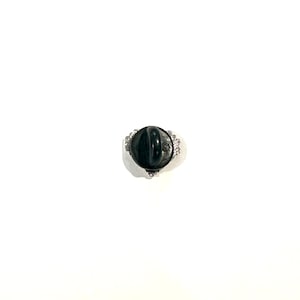 Puede incluir: Un prendedor negro con un borde decorativo plateado. La parte trasera del prendedor es redonda con un dise&ntilde;o acanalado y un cierre. El borde tiene peque&ntilde;os adornos redondos y transparentes.