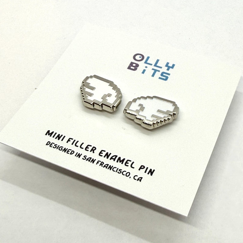 Puede incluir: Dos mini alfileres de esmalte de relleno con forma de nube pixelada, con centro blanco y contorno plateado, expuestos sobre una tarjeta blanca. La tarjeta presenta el texto "Olly Bits" y "Mini Filler Enamel Pin Designed in San Francisco, CA."