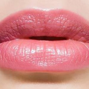 May include: Close-up of a person's lips wearing a light pink lipstick. The lipstick has a glossy finish.