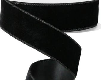 Puede incluir: Un carrete de cinta de terciopelo negro con reverso de satén. La cinta mide aproximadamente 2.5 cm de ancho y tiene un borde cosido. La cinta está enrollada alrededor de un carrete de cartón blanco.