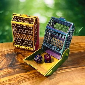 May include: Two colourful dice towers with a honeycomb design. The towers are made of plastic and have a purple and blue colour scheme. The towers are open and show a purple and blue dice inside. The dice are numbered 6 and 20.