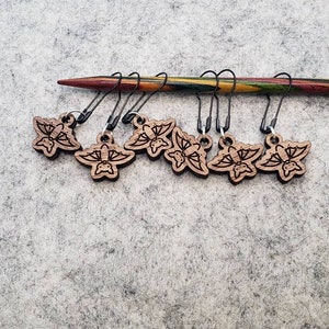 May include: Set of seven wooden stitch markers with butterfly designs. Each marker has a black metal loop and a brown wooden butterfly charm.
