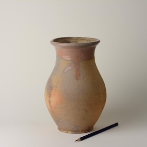 May include: A rustic, handcrafted vase with a wide base and a slightly flared rim. The vase features a warm color palette of earthy tones, including browns, tans, and a touch of orange. A dark blue pencil rests beside the vase.