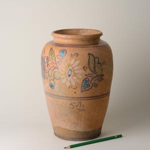 May include: A large, antique terracotta vase with hand-painted floral and butterfly designs in pastel colors. The vase has a wide body, a narrow neck, and a slightly flared rim. The vase has a rustic, aged appearance, with visible wear and tear.