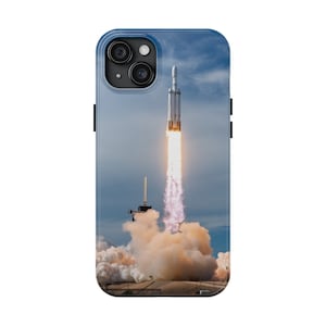 May include: A white rocket with a plume of fire and smoke launches into a blue sky with white clouds.
